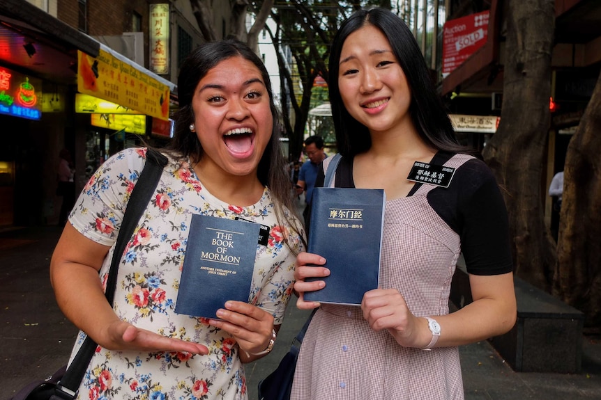 Mormon missionaries Sister Wolfgram (L) and Sister Lu (R) holding The Book of Mormon.