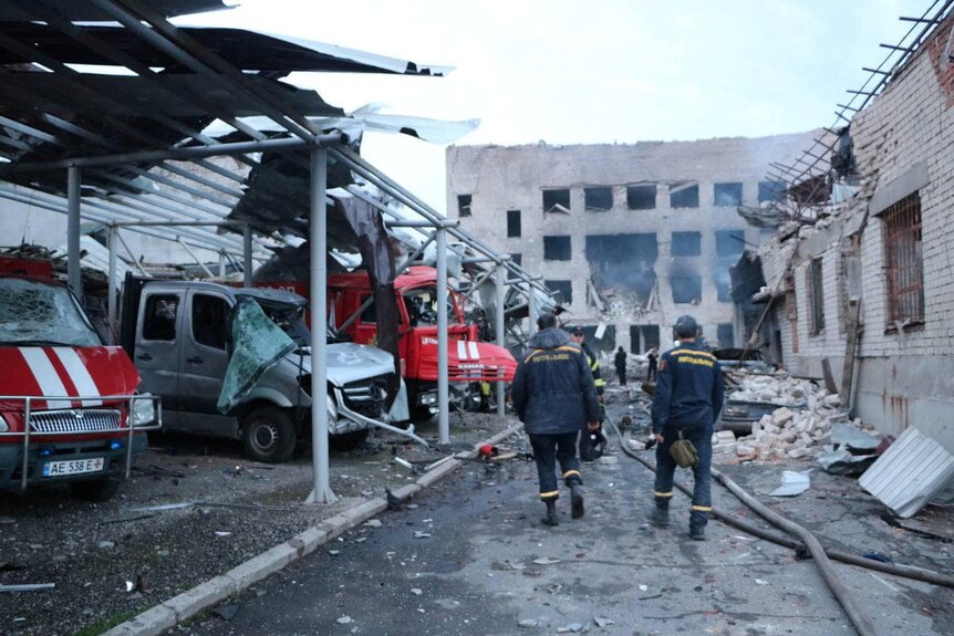 Rescuers walk past destroyed vehicles and damaged brick buildings inside a firefighters' depot.