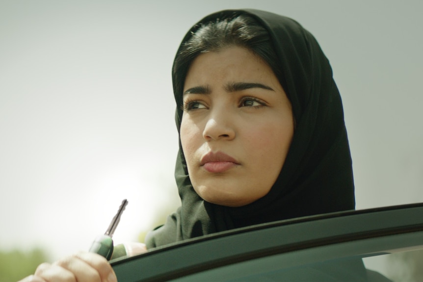 Film still of Mila Al Zahrani as Maryam standing above a car window in The Perfect Candidate