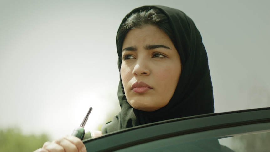 Film still of Mila Al Zahrani as Maryam standing above a car window in The Perfect Candidate