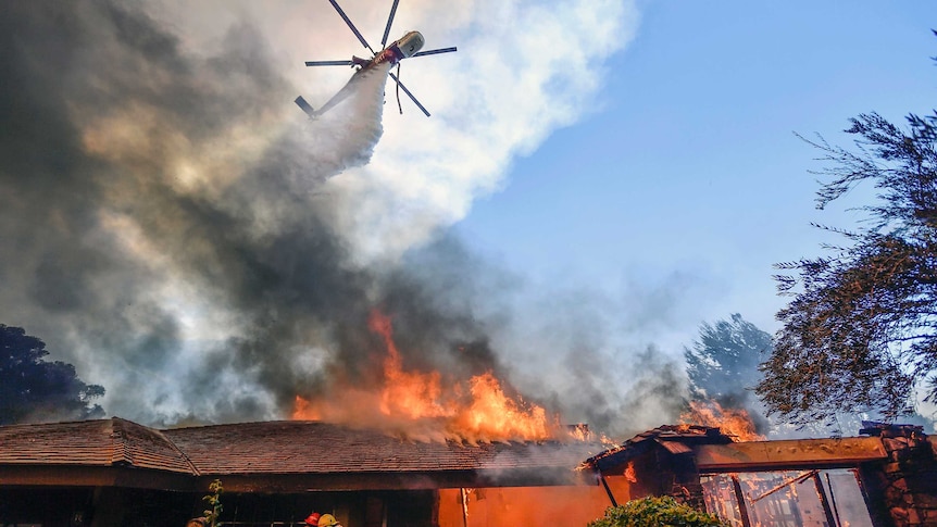 A helicopter dumps water over a burning house.