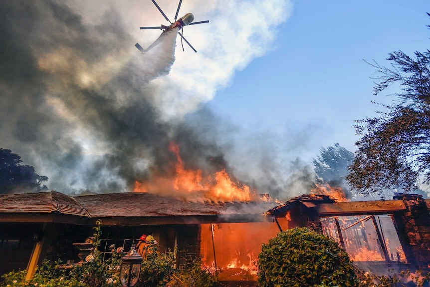 A helicopter dumps water over a burning house.