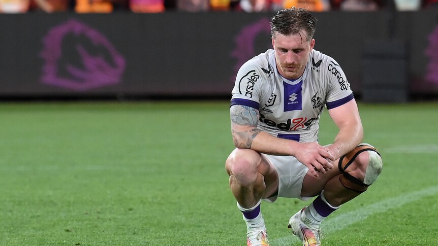 Melbourne Storm's Cameron Munster squats on the grass after a loss to Brisbane Broncos.