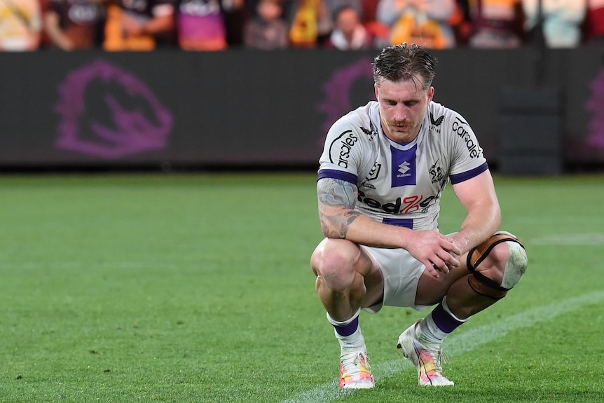 Melbourne Storm's Cameron Munster squats on the grass after a loss to Brisbane Broncos.