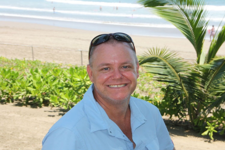 A man wearing a blue shirt standing on a beach 