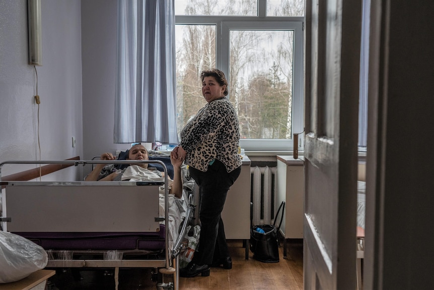Matka trzyma rękę rannego syna na oddziale szpitalnym na Ukrainie.