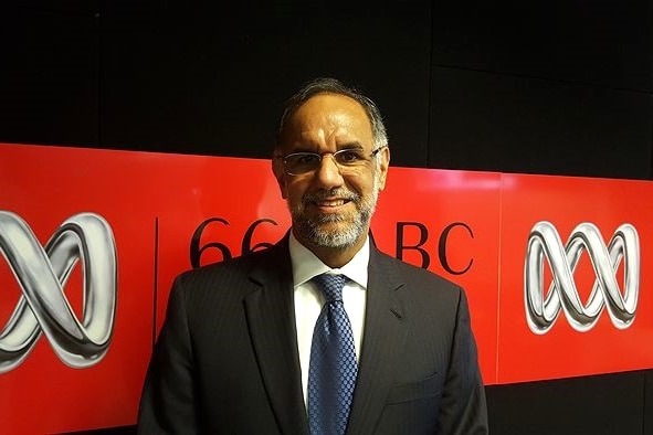 Navdeep Suri wearing a suit and glasses standing in front of an ABC Canberra sign. 