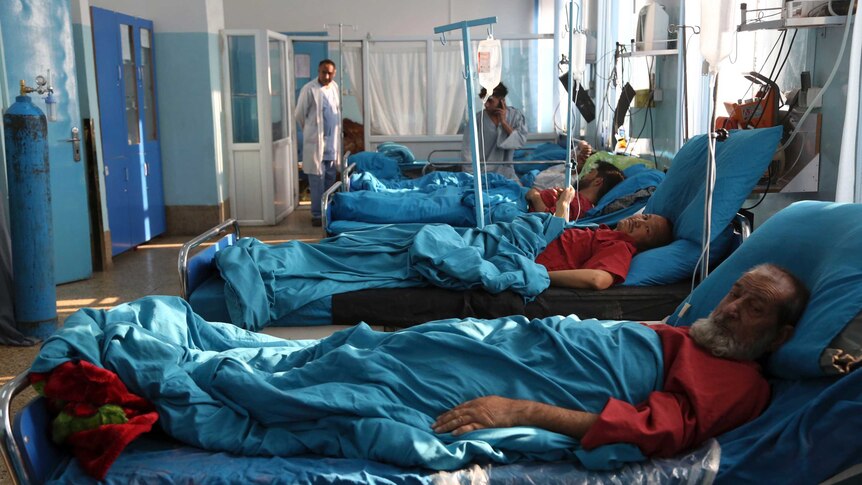 Men in red shirts lie in hospital beds with blue linen.