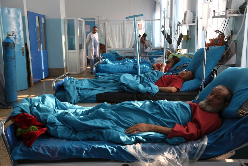 Men in red shirts lie in hospital beds with blue linen.
