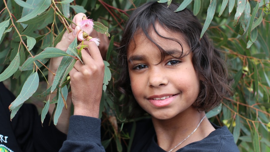 A smiling Indigenous girl amid some greenery.