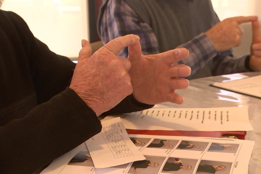 A close up photo of two elderly people's hands as they use sign language.