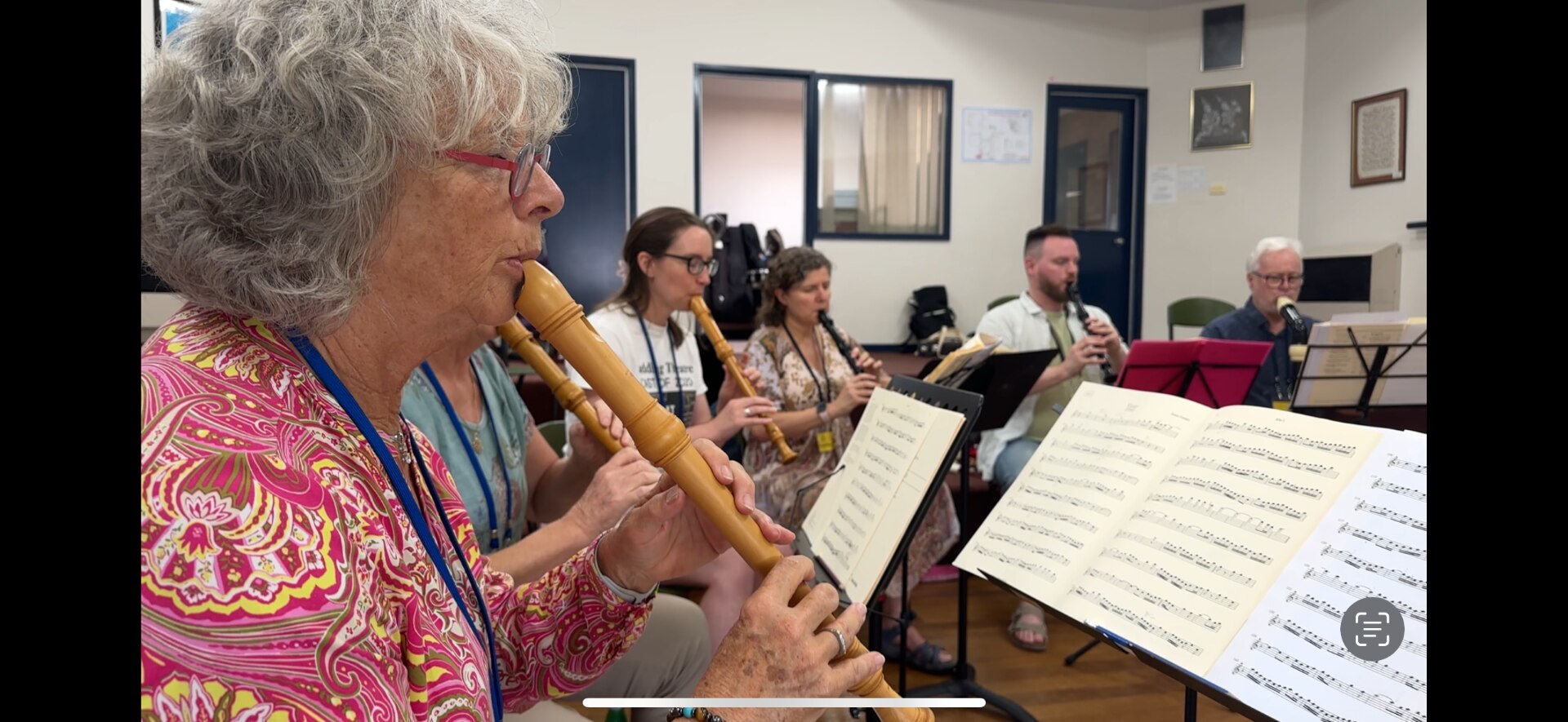 An elderly woman plays along from sheet music with the recorder 