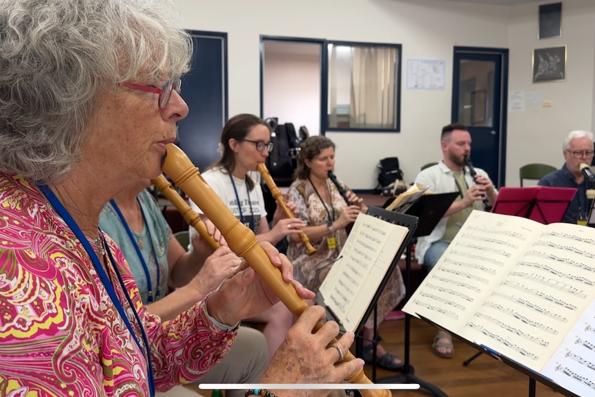 An elderly woman plays along from sheet music with the recorder 