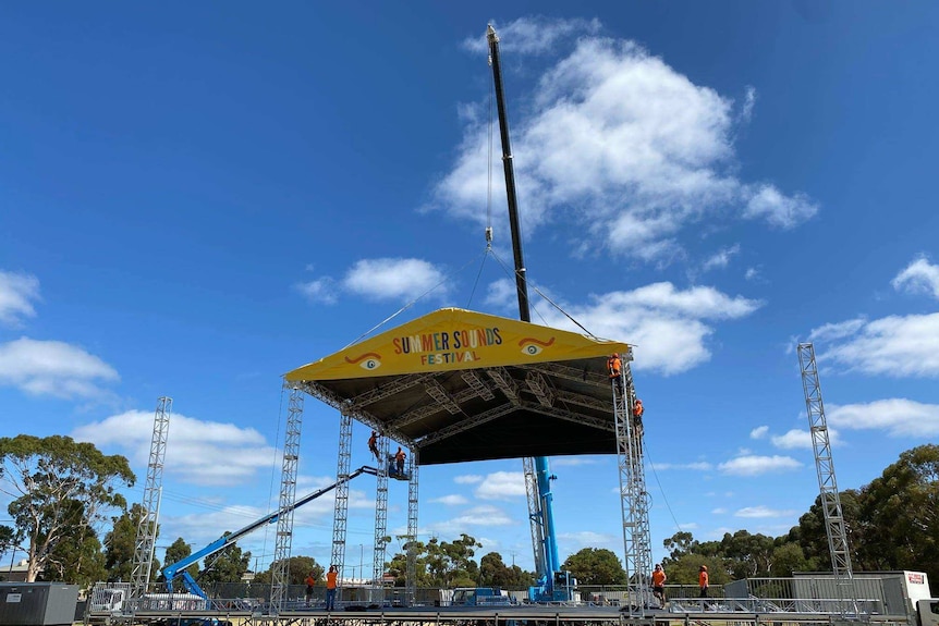 A concert stage being lowered into place by a crane in a park