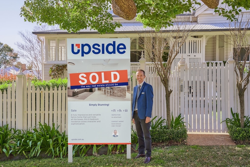 A man standing next to a sold sign