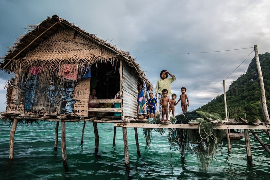 Children stand on the deck of a home on stilts over the water.