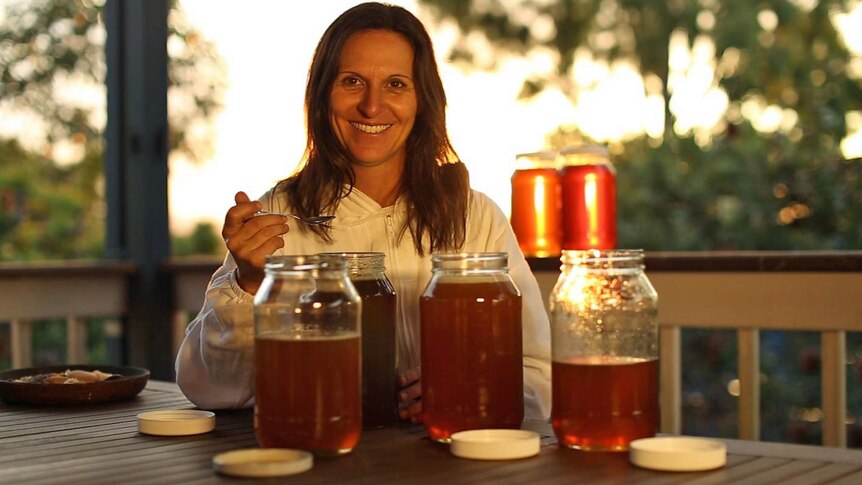 Laura Ellis sits on her deck bottling her backyard honey in large glass jars.