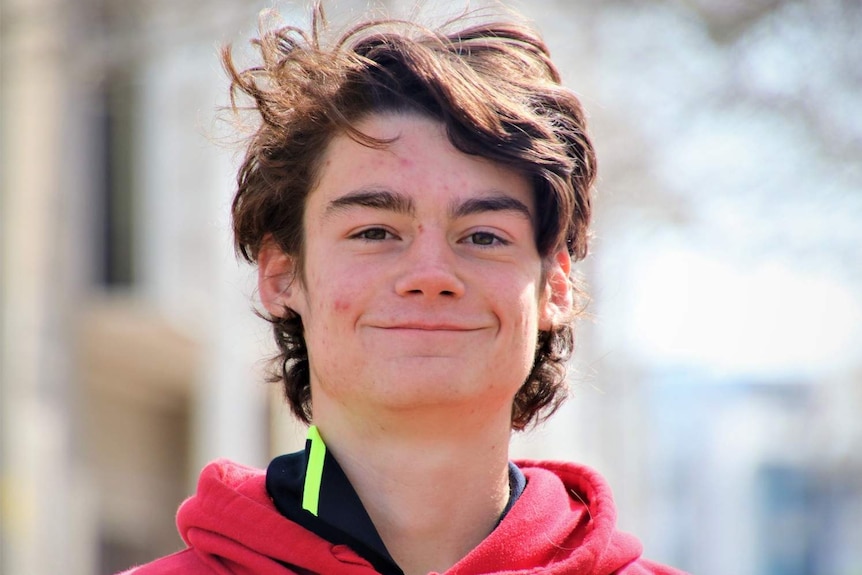 A close up of Luke Klumpp smiling, wearing a red jumper.