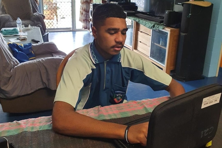 Teenage boy in school uniform sitting in front of a laptop