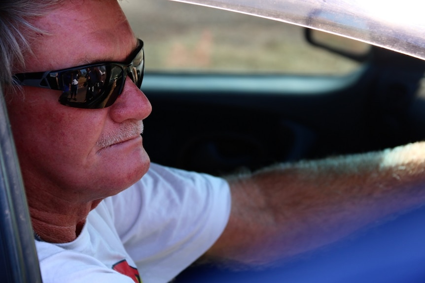 Don is wearing sunglasses and a while shirt, and is pictured in the drivers seat of a car