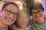 Two women wearing glasses smiling with a blurred face of a child