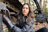 Woman with brown hair locked onto a large logging machine with 'forests' and 'life' written on her arms