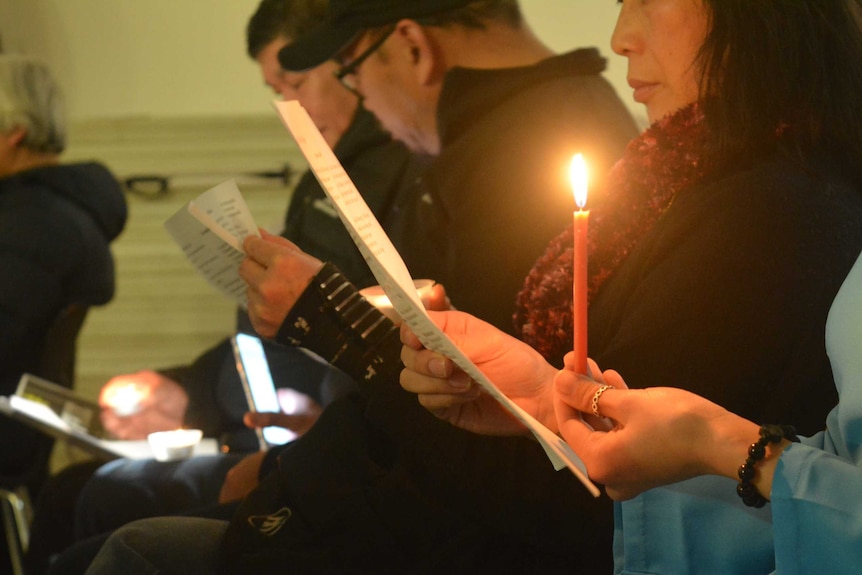 A woman holds a candle and reads music