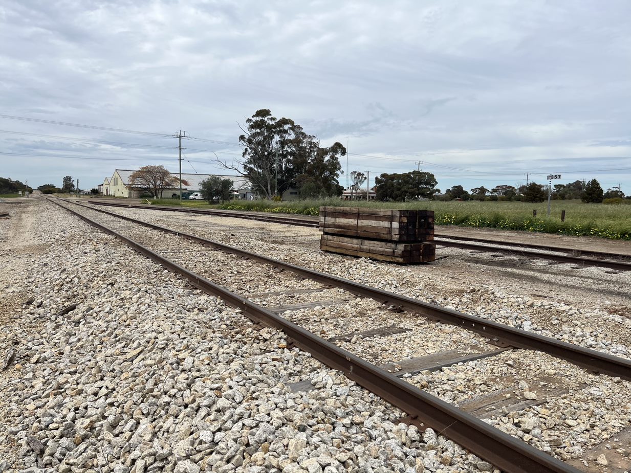 An empty train track in regional Victoria with wood on the track and a farm behind it