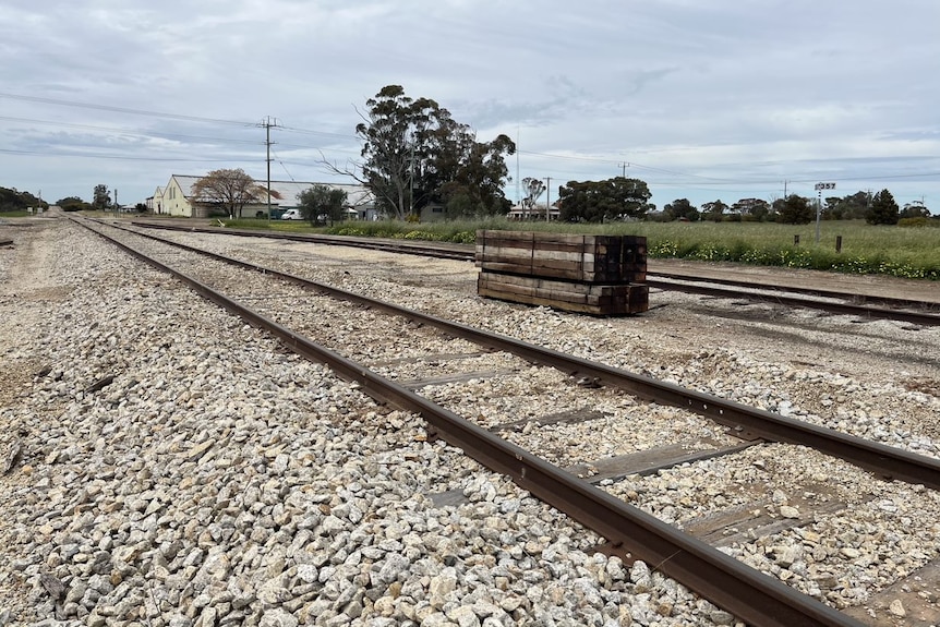 An empty train track in regional Victoria with wood on the track and a farm behind it