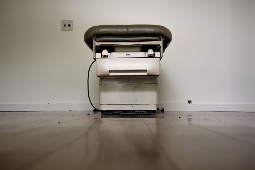 An examination table sits in an otherwise empty room, unplugged 