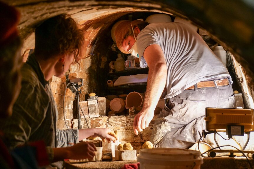Two potters carefully select works to stack and pack in the wood fired kiln. 