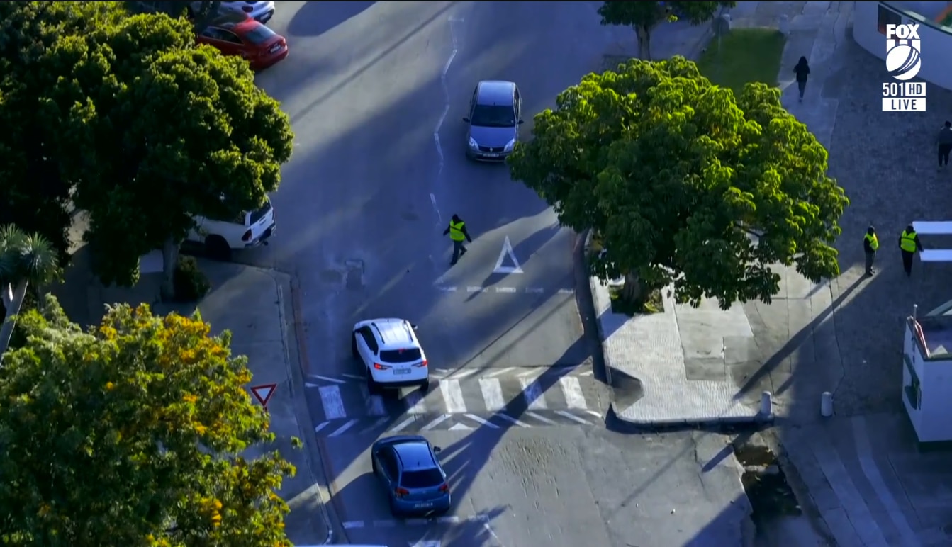 A man in high-vis collects a ball on a road with cars on it