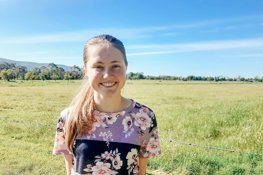 a young woman stands in a paddock smiling
