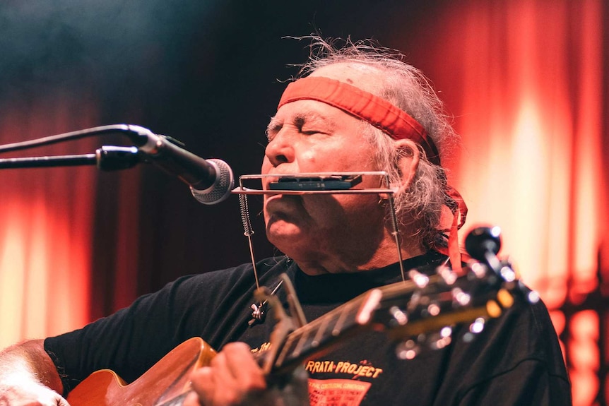 Kev Carmody plays a harmonica onstage at Bluesfest 2022