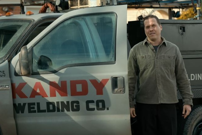 A man stands next to a truck with the words "Kandy Welding Co" on it.