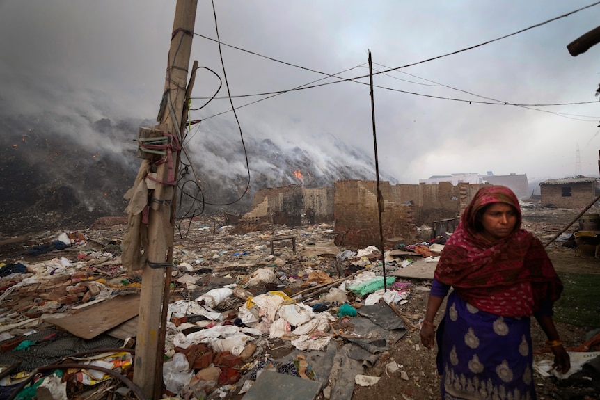 O femeie care locuiește la marginea unei gropi de gunoi din Bhalswa trece pe lângă un incendiu