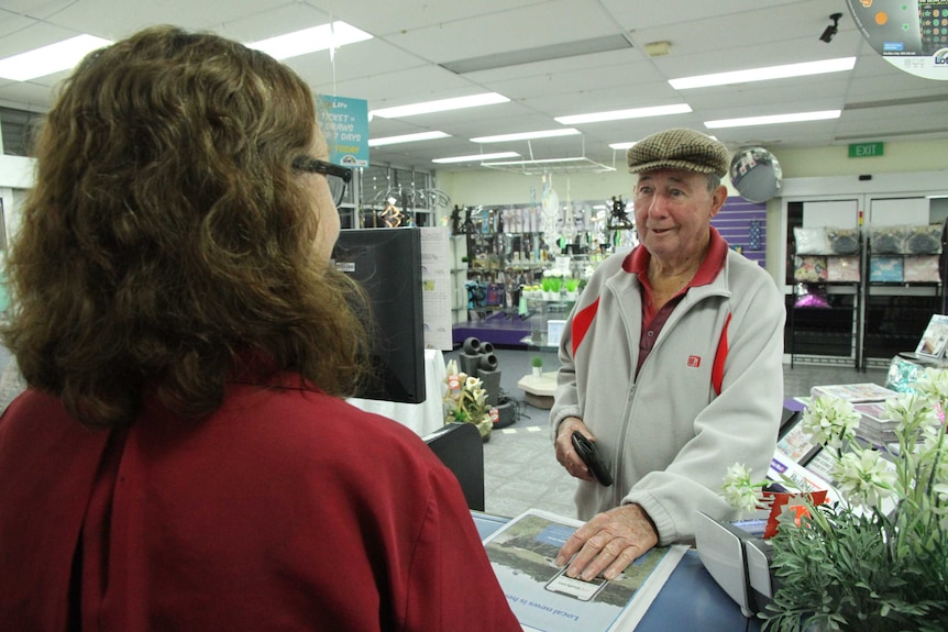 An elderly gentleman buys a newspaper from a woman at a newsagent