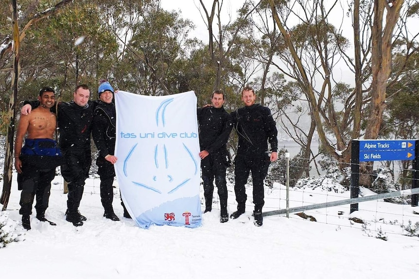 Diver club members in the snow stand in the snow holding a club sign