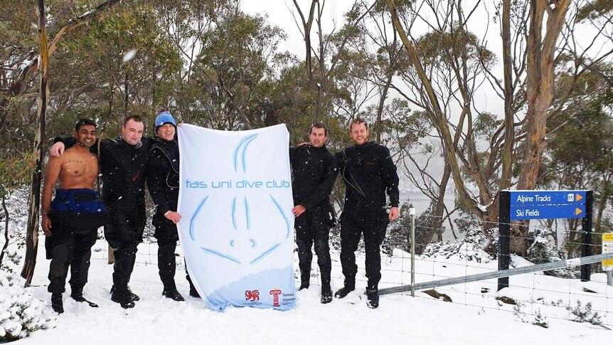 Diver club members in the snow stand in the snow holding a club sign