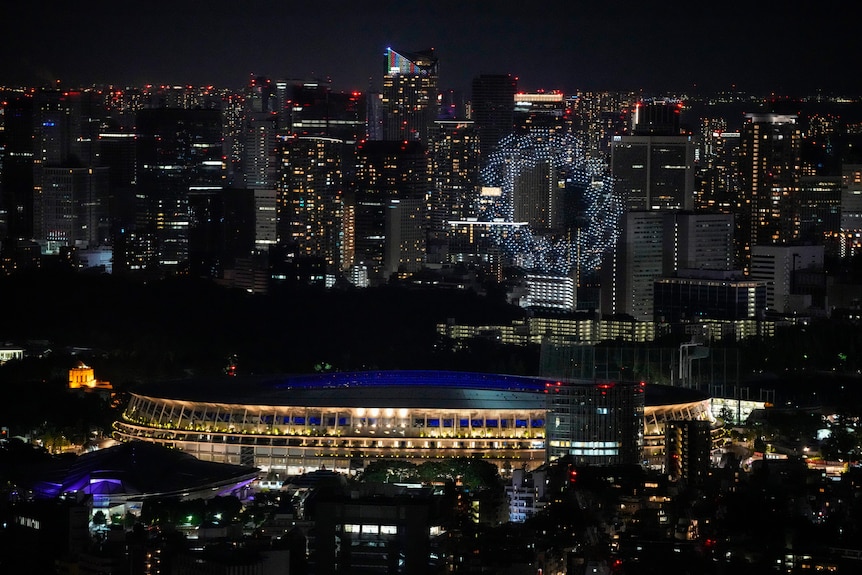 More than 1,800 drones form the shape of the Tokyo 2020 logo above a city stadium.