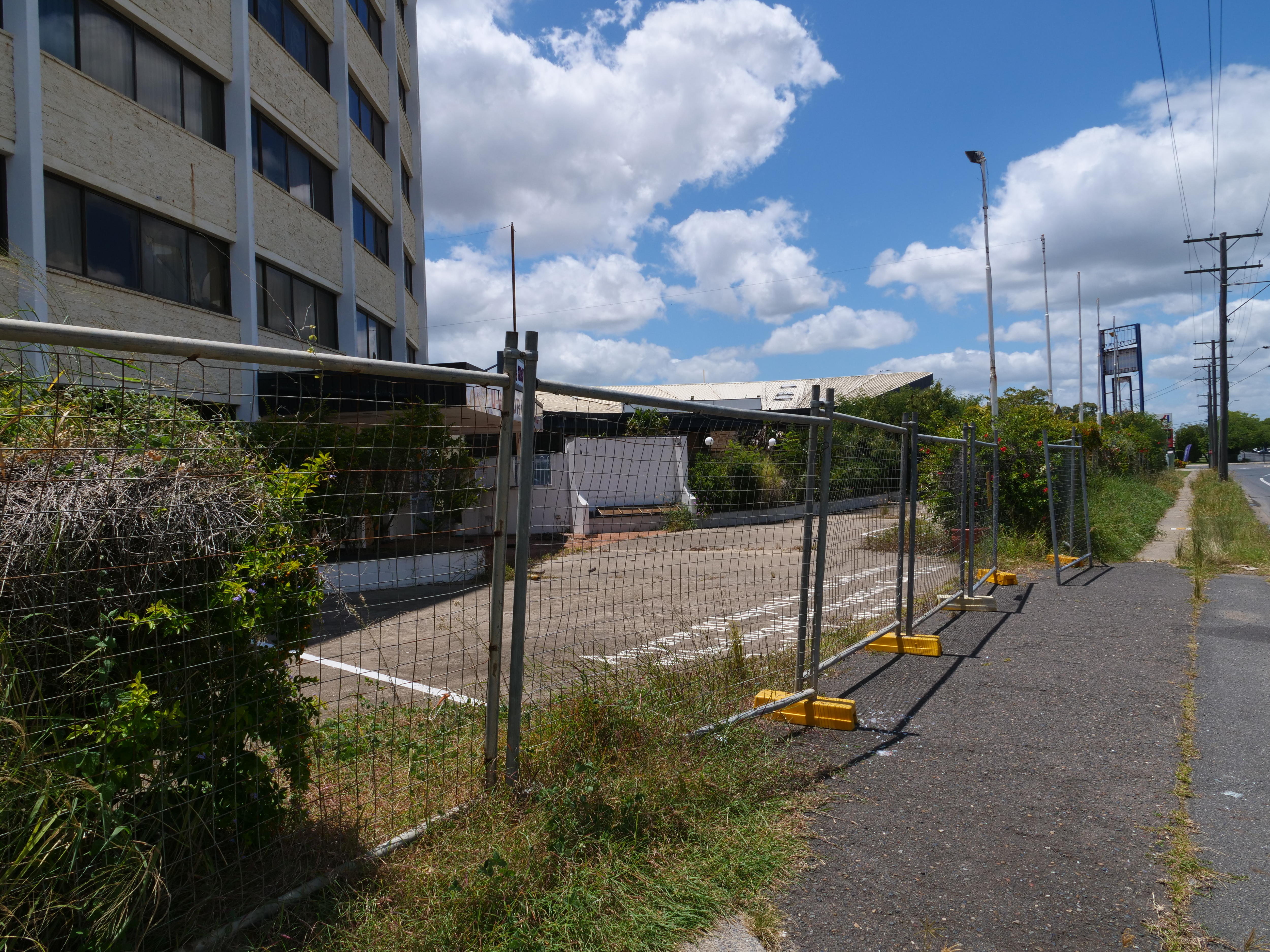 Jardines cubiertos de maleza rodeados de vallas y edificio de motel de hormigón abandonado