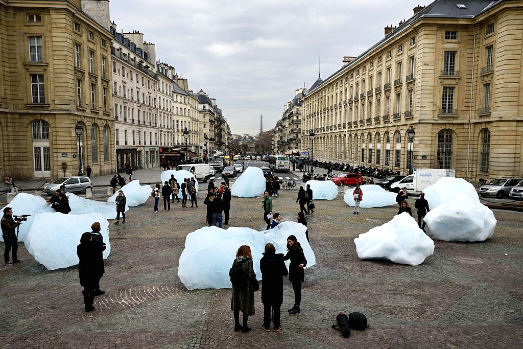 People looking at chunks of ice almost their height, on a Paris street with the Eiffel Tower in the background