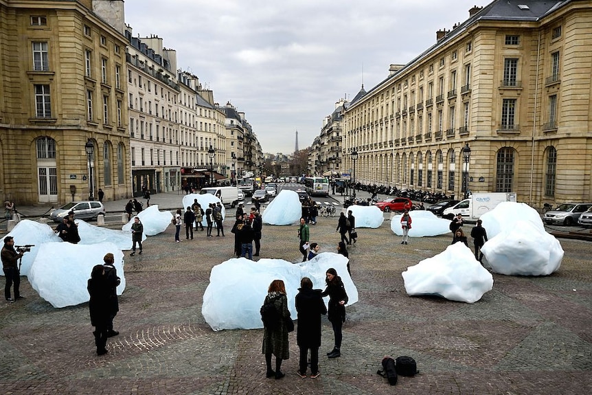 People looking at chunks of ice almost their height, on a Paris street with the Eiffel Tower in the background