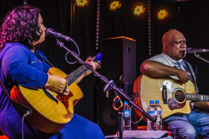 Nancy Bates and Archie Roach perform on stage holding guitars.