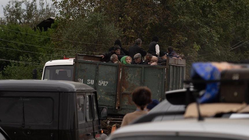 group of people in back of a large truck on dirt road surrounded by cars