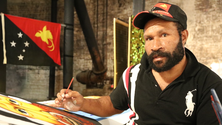 A man painting with the PNG flag behind him.