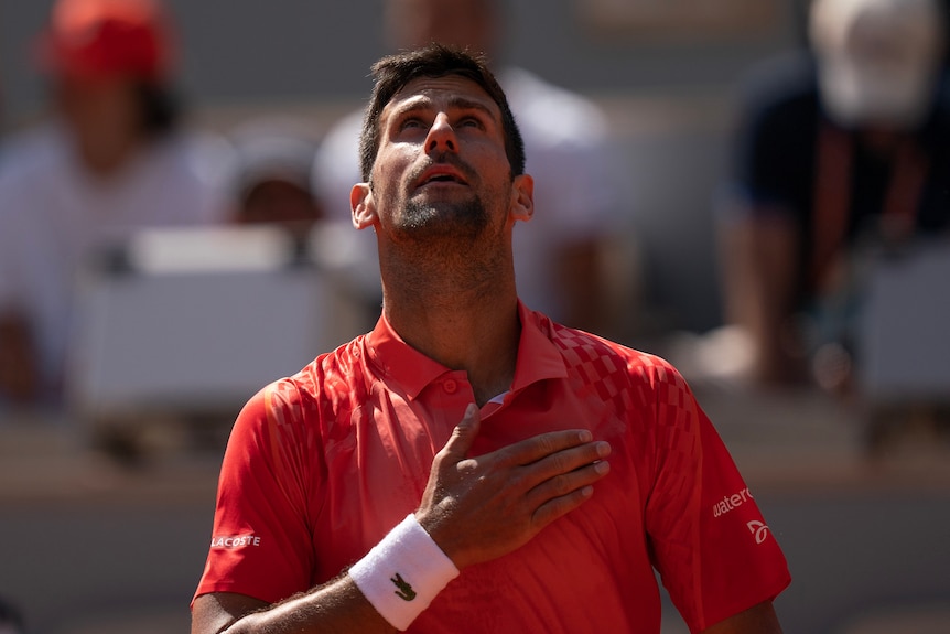 A man in a red shirt with his hand to his chest, looking up.