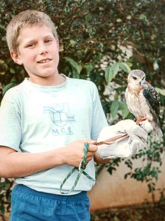 A boy wearing a tshirt and shorts holds a bird on his arm