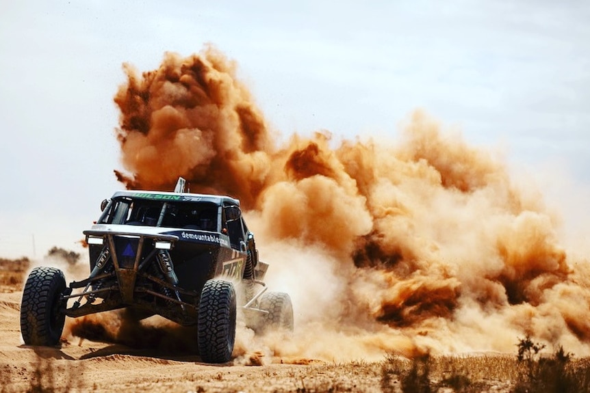 A modified four wheel drive travelling through a cloud of dirt