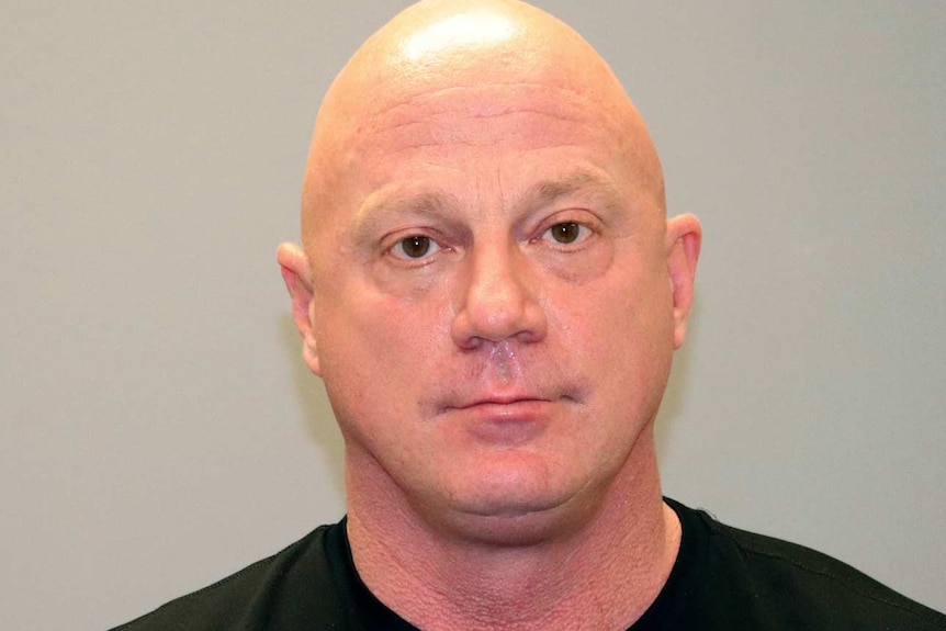 a mugshot of Larry Rendall Brock Jr wearing a black shirt with a shaved head